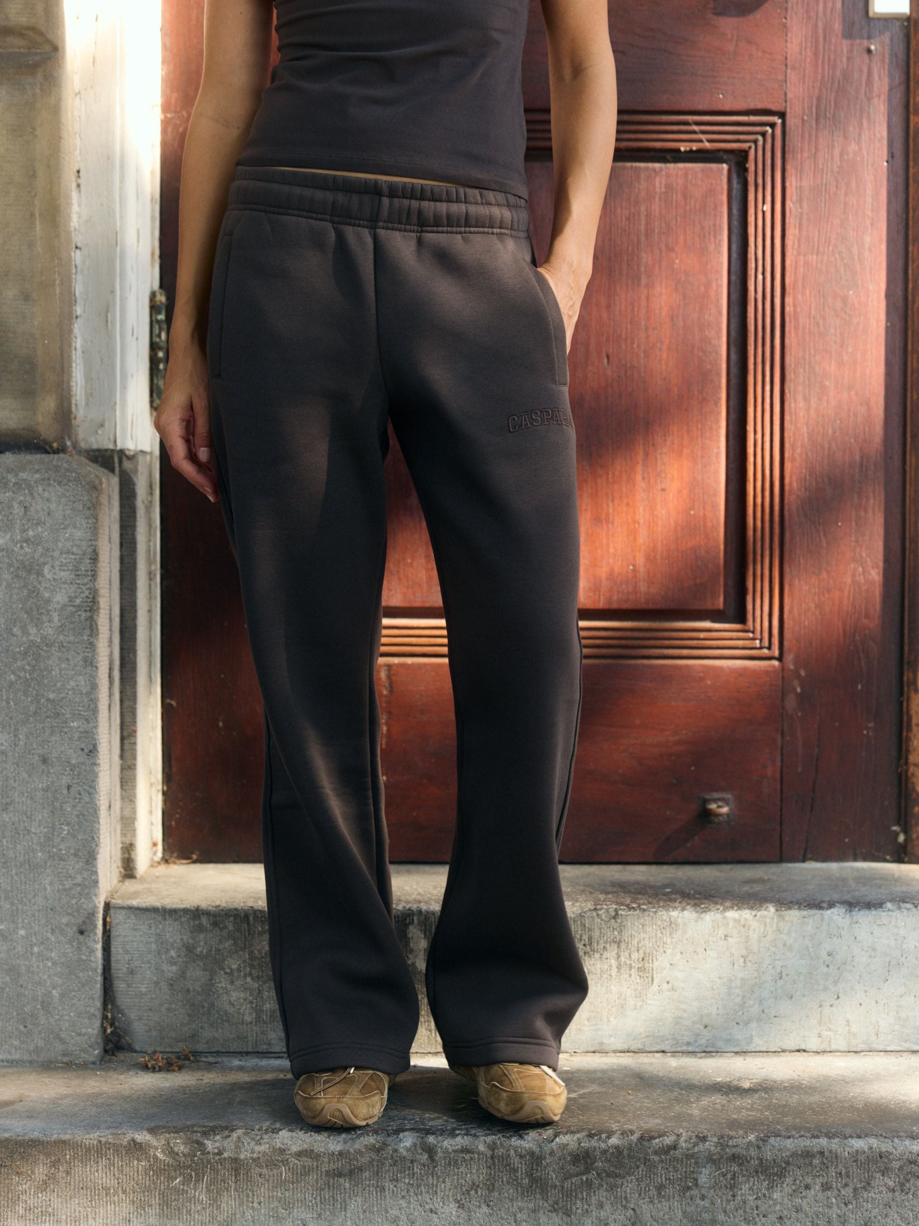Woman wearing espresso straight-leg sweatpants standing on stone steps in front of a wooden door.